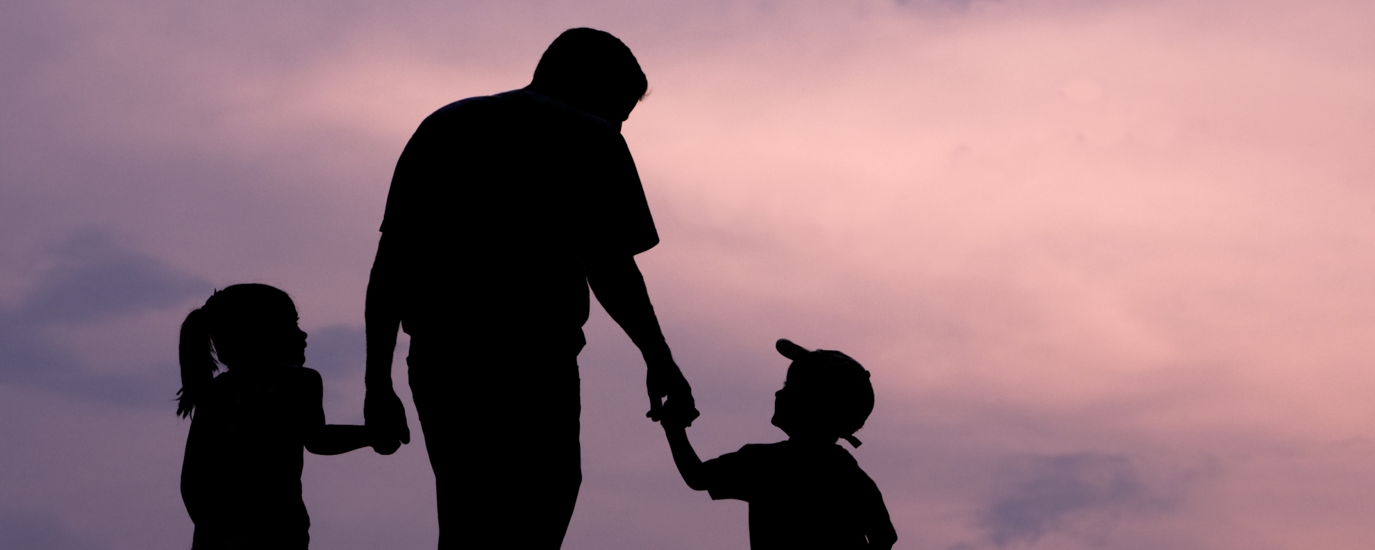 Silhouette of father walking with two kids against pink and purple sky